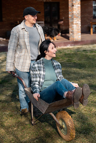 Man pushing smiling woman in wheelbarrow at their affordable home in Franklin County